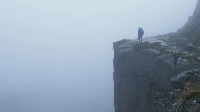 Man doing extreme hiking at Pulpit Rock in foggy Norway morning