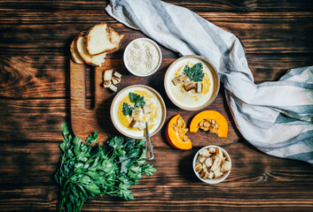 two plates with pumpkin soup near vegetables pumpkin greens with breadcrumbs on a wooden dark table top view vegetarian healthy food