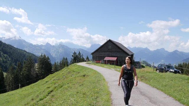 Pretty woman hiking on rural path during sunny day with beautiful alp mountains in background.Amden,Switzerland.Track shot.