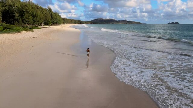 Tan man running on beach at sunrise in Hawaii with waves crashing