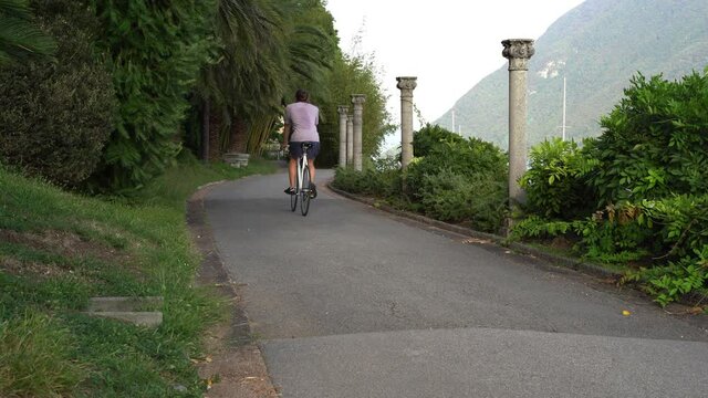 Guy drives a single-speed bicycle in his beautiful garden hallway surrounded by green nature and mountains.