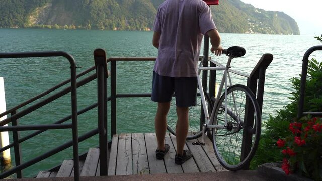 Guy reaches his destination and leaves his bike open on the deck nearby a lake to go to on adventures.