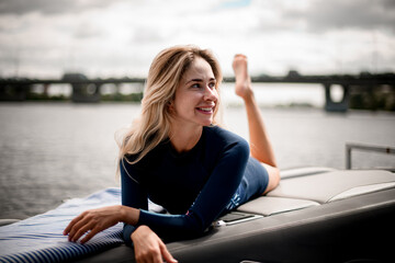 Fototapeta na wymiar Beautiful young smiling woman with in wetsuit lies on the boat.