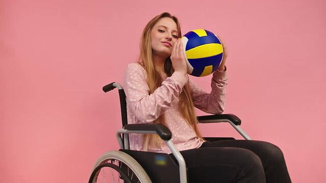 Profile of Young Paralympian Woman in Wheelchair Holding Volley Ball and Posing. Positive Handicapped Person Lifestyle Concept, Static Full Frame Isolated on Pink Background