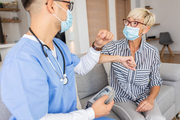 Male nurse greeting with senior female patient with mask while being in a home visit.
