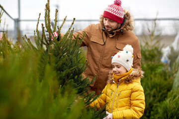 family, winter holidays and people concept - happy father and little daughter choosing christmas tree at street market