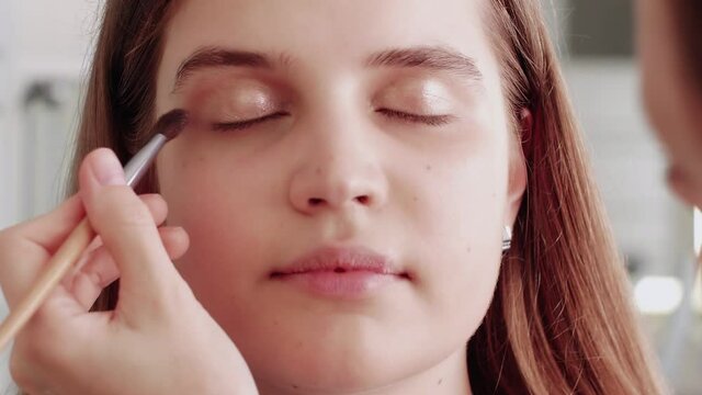 Professional make up artist makes blush on model's face using makeup brush.