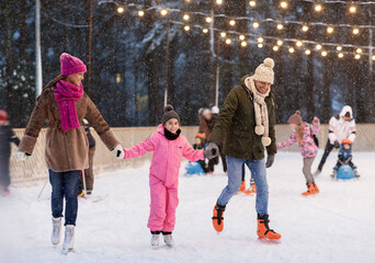 christmas, family and leisure concept - happy mother, father and daughter at outdoor skating rink...