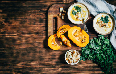 Obraz na płótnie Canvas two plates with pumpkin soup near vegetables pumpkin greens with breadcrumbs on a wooden dark table top view vegetarian healthy food 