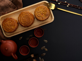Top view of dark modern table with tea set, moon cakes on wooden tray, decoration and copy space