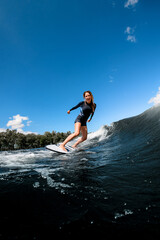 happy young woman in swimsuit rides down the wave on surfboard