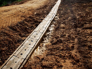 Concreate drainage covered by lids. On the side of the road being built on a wet ground background....