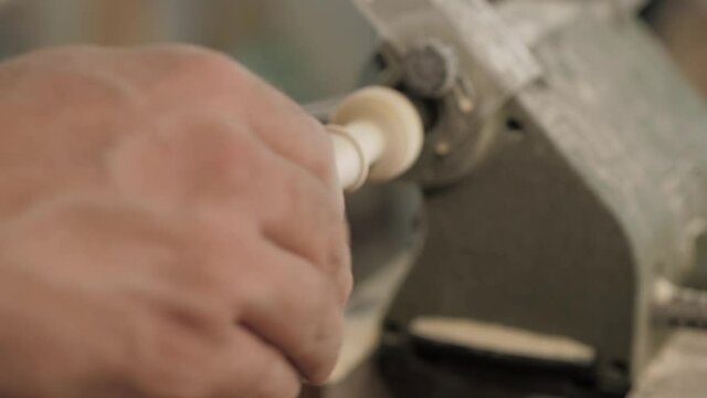 Close-up of a professional carpenter using sandpaper to grind a piece of wood on a lathe.