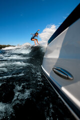 view on young woman in who riding on surfboard on wave from motor boat