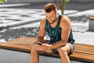 fitness, sport and technology concept - young athlete man with earphones and smartphone listening to music outdoors