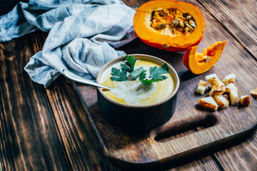 a plate of pumpkin soup on a background of pumpkin and bread crumbs on a dark wooden table