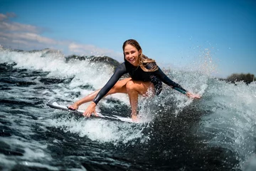 Foto op Plexiglas smiling girl having fun sitting on surf board and touching the water with her hand. © fesenko