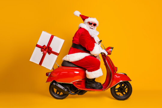 Full length profile side photo of grey white hair bearded santa claus ride drive bike deliver gift box x-mas christmas night wear red headwear isolated yellow color background