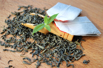 Tea bags and a wooden spoon with fresh mint leaves lie on a heap of tea on a wooden background