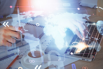 Double exposure of world map hologram with man working on computer on background. Concept of worldwideweb.