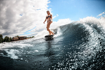 beautiful woman in swimsuit stands on surfboard and rides down the wave