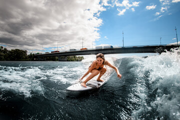 Naklejka premium Active girl having fun sitting on surf board and touching the water with her hand.
