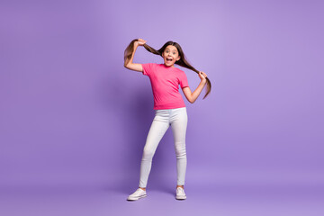 Fototapeta na wymiar Full length body size photo of funny small girl holding long brunette hair grimacing isolated on purple color background