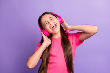 Fototapeta premium Photo portrait of pretty cute little girl holding pink earphones singing song listening to favourite music isolated on purple color background
