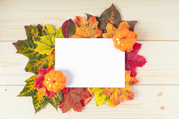 Orange pumpkins, maple leaf, berries and mock up paper blank on wooden background. Hello Fall greeting card, autumn time concept. Flat lay. Copy space