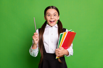 Photo portrait of schoolgirl with open mouth holding pen notebooks isolated on vivid green colored background