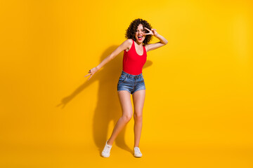 Fototapeta na wymiar Full length body size photo of pretty female hipster with curly hairdo dancing moving smiling showing gesture v-sign with two fingers at party isolated on vivid yellow color background