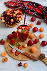 Still life of strawberries, plums, cherries and a glass with berry juice on a cutting board on a light wooden table