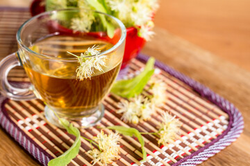 glass cup of herbal drink, linden extract tea, linden tree flowers are around the cup, alternative medicine, wellness concept