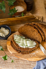 Rye whole grain bread slices with butter, fresh cucumber and salt on wooden table, country organic healthy sandwich, home kitchen, rustic style. Selective focus with copy space.