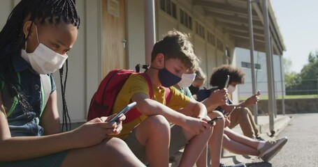 Group of kids wearing face masks using smartphones while sitting together - Powered by Adobe