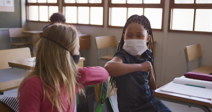 Two girls wearing face masks greeting each other by touching elbows at school