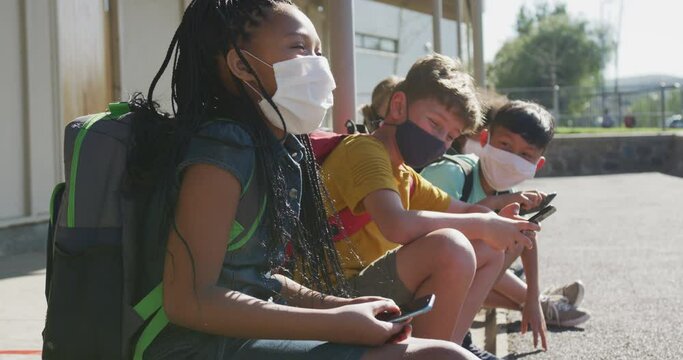 Group of kids wearing face masks using smartphones while sitting together