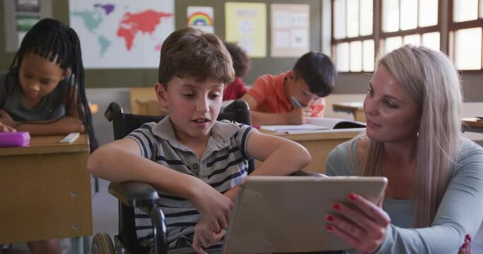 Female teacher teaching disable boy by using digital tablet at school