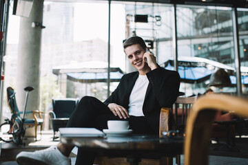 Smiling man with smartphone sitting at table in cafe