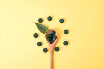 spirulina in tablets with wood spoon and jar on yellow background. Concept natural, eco, powder healthy dietary supplement