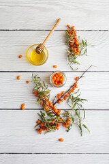 Table top view with sea buckthorn berries on branch with honey at white wood background