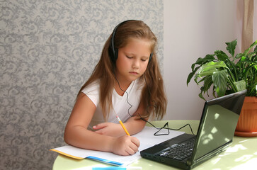Focused kid self isolation wearing headphones using laptop in cafe, writing notes,student girl...
