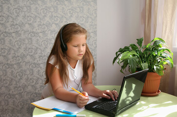 Focused kid self isolation wearing headphones using laptop in cafe, writing notes,student girl...