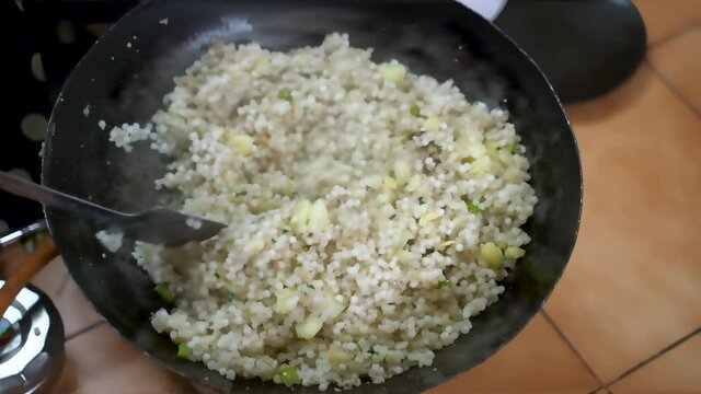 Sabudana Khichdi-Sago Polenta In A Big Deep Metal Pan (Kadai) Stirred Using Stainless Flat Ladle To Cook Over A Stove. - Close Up-topdown Shot