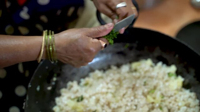 Garnishing The Sabudana Khichdi - Sago Polenta Cuisine By Slicing Fresh Coriander Using Small Knife In A Kadai. - High Angle Shot