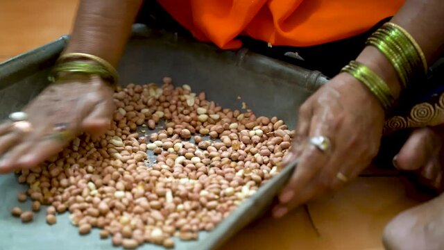 Indian Lady Peeling-Off Nut's Skin In A Winnowing Basket By Pressing And Squeezing It Using Her Palm. - High Angle Shot 