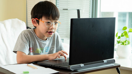 On Asian boy student is learning online class and studying by video call. The happy boy learns english language with laptop at home.New normal.Covid-19 coronavirus, social distancing and staying home. © Natcharlai