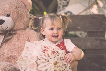 Süßes Kleinkind Mädchen mit rotem Kleid und Zöpfen großer Teddybär Sonnenschirm lächelt...