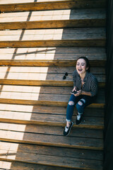 Caucasian female blogger with modern cellphone in hand resting at urban stairs grinning and...