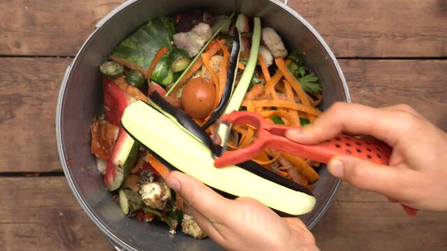 Reduce food loss and waste. Housewife throws vegetable peeling, scraps and fruit peels in compost bucket. Top view. Organic kitchen home waste gathering for composting